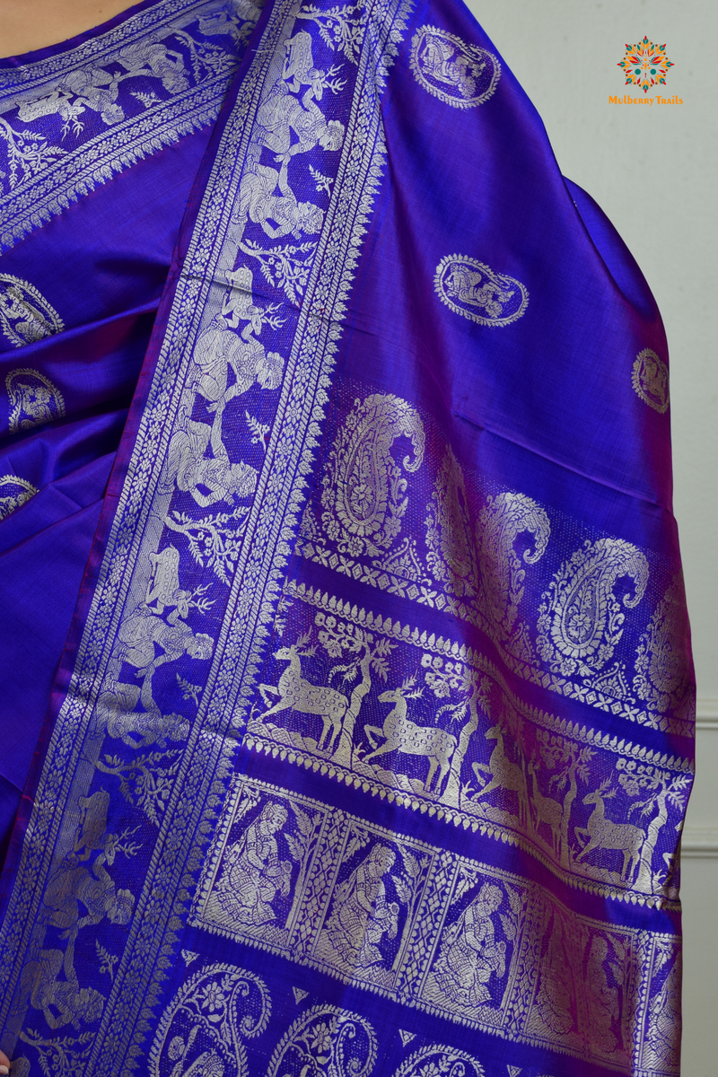 A woman wearing a Purple Baluchari Pure SIlk saree. Purple baluchari silk , bengal silk saree with deer motif on pallu and ramayan, mahabharat motifs on pallu. This is a soft pure silk saree suitable for weddings, parties, festivities. suitable for Durga Puja shopping enthusiasts and diwali festival. 