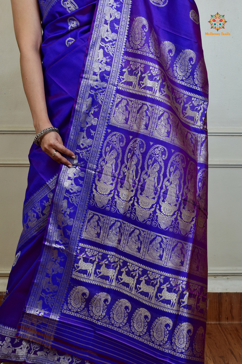 A woman wearing a Purple Baluchari Pure SIlk saree. Purple baluchari silk , bengal silk saree with deer motif on pallu and ramayan, mahabharat motifs on pallu. This is a soft pure silk saree suitable for weddings, parties, festivities. suitable for Durga Puja shopping enthusiasts and diwali festival. 