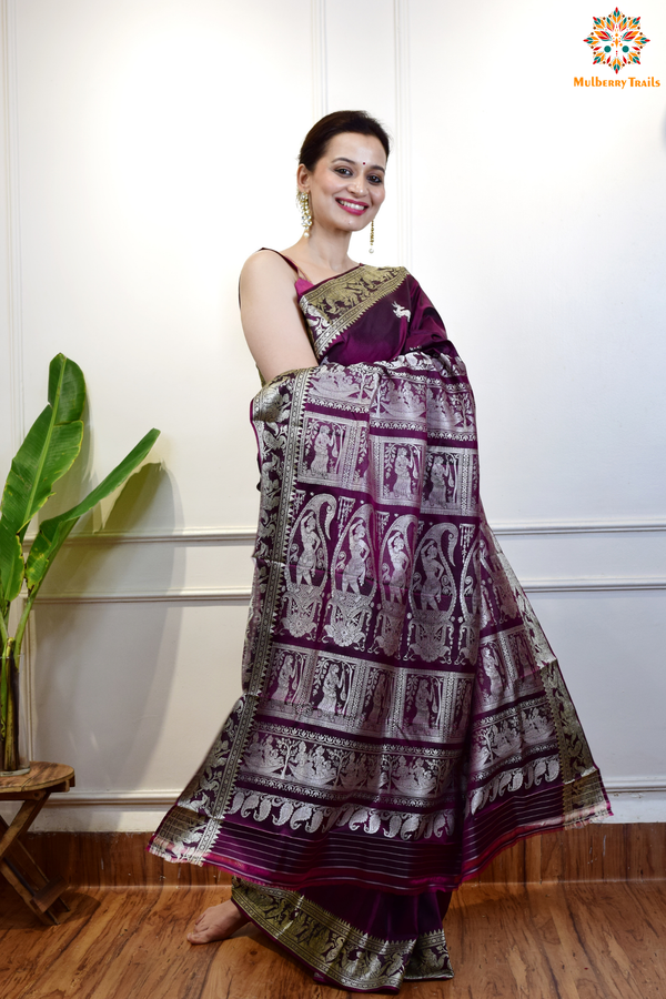 A woman wearing a Purple Baluchari Pure SIlk saree. Purple baluchari silk , bengal silk saree with deer motif on pallu and ramayan, mahabharat motifs on pallu. This is a soft pure silk saree suitable for weddings, parties, festivities. suitable for Durga Puja shopping enthusiasts and diwali festival. 