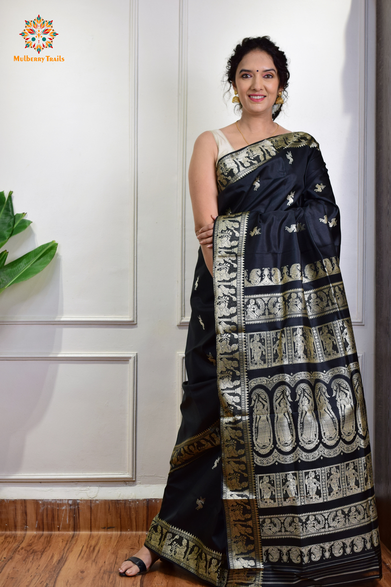 A woman wearing a black Baluchari Pure SIlk saree. Black baluchari silk , bengal silk saree with deer motif on pallu and ramayan, mahabharat motifs on pallu. This is a soft pure silk saree suitable for weddings, parties, festivities. suitable for Durga Puja shopping enthusiasts and diwali festival. 