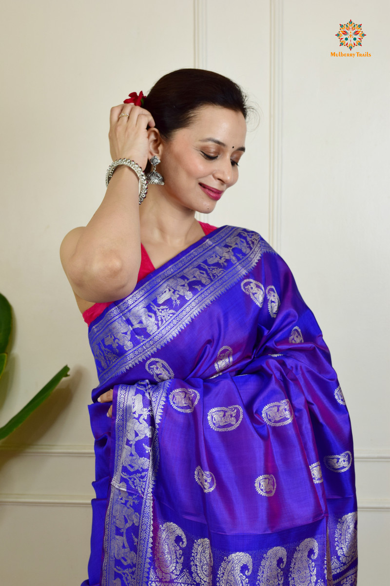 A woman wearing a Purple Baluchari Pure SIlk saree. Purple baluchari silk , bengal silk saree with deer motif on pallu and ramayan, mahabharat motifs on pallu. This is a soft pure silk saree suitable for weddings, parties, festivities. suitable for Durga Puja shopping enthusiasts and diwali festival. 