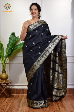 A woman wearing a black Baluchari Pure SIlk saree. Black baluchari silk , bengal silk saree with deer motif on pallu and ramayan, mahabharat motifs on pallu. This is a soft pure silk saree suitable for weddings, parties, festivities. suitable for Durga Puja shopping enthusiasts and diwali festival. 