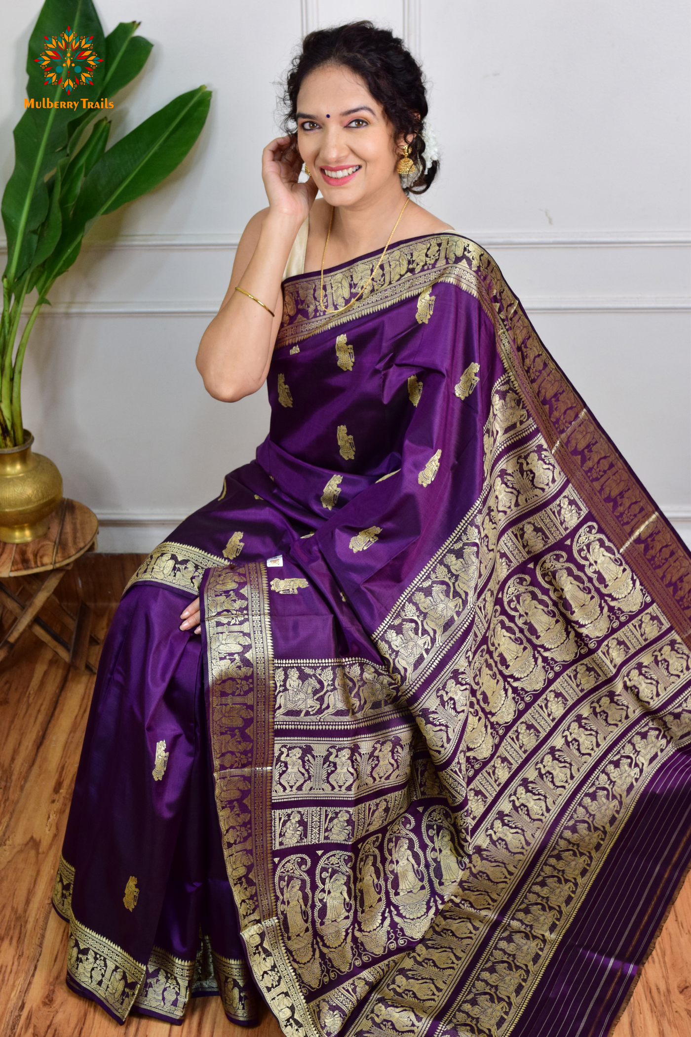 A woman wearing a Purple Baluchari Pure SIlk saree. purple baluchari silk , bengal silk saree with deer motif on pallu and ramayan, mahabharat motifs on pallu. This is a soft pure silk saree suitable for weddings, parties, festivities. suitable for Durga Puja shopping enthusiasts and diwali festival. 