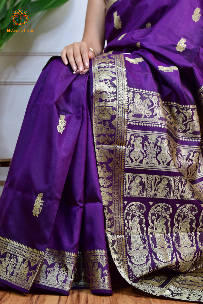 A woman wearing a Purple Baluchari Pure SIlk saree. purple baluchari silk , bengal silk saree with deer motif on pallu and ramayan, mahabharat motifs on pallu. This is a soft pure silk saree suitable for weddings, parties, festivities. suitable for Durga Puja shopping enthusiasts and diwali festival. 