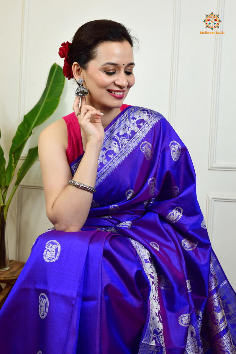 A woman wearing a Purple Baluchari Pure SIlk saree. Purple baluchari silk , bengal silk saree with deer motif on pallu and ramayan, mahabharat motifs on pallu. This is a soft pure silk saree suitable for weddings, parties, festivities. suitable for Durga Puja shopping enthusiasts and diwali festival. 