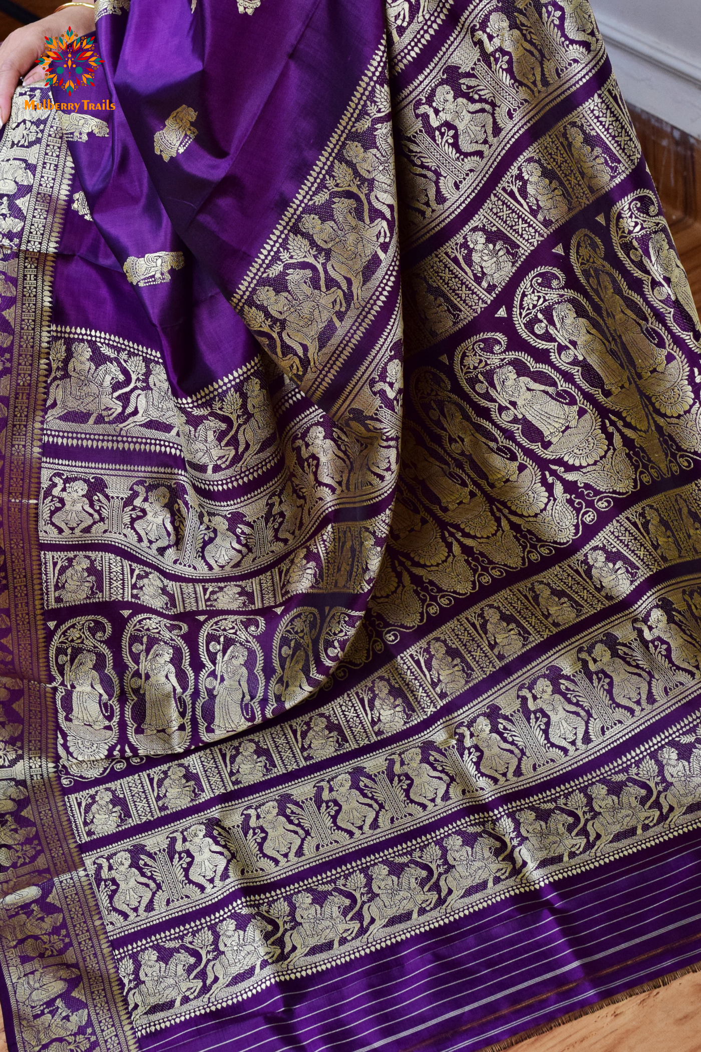 A woman wearing a Purple Baluchari Pure SIlk saree. purple baluchari silk , bengal silk saree with deer motif on pallu and ramayan, mahabharat motifs on pallu. This is a soft pure silk saree suitable for weddings, parties, festivities. suitable for Durga Puja shopping enthusiasts and diwali festival. 