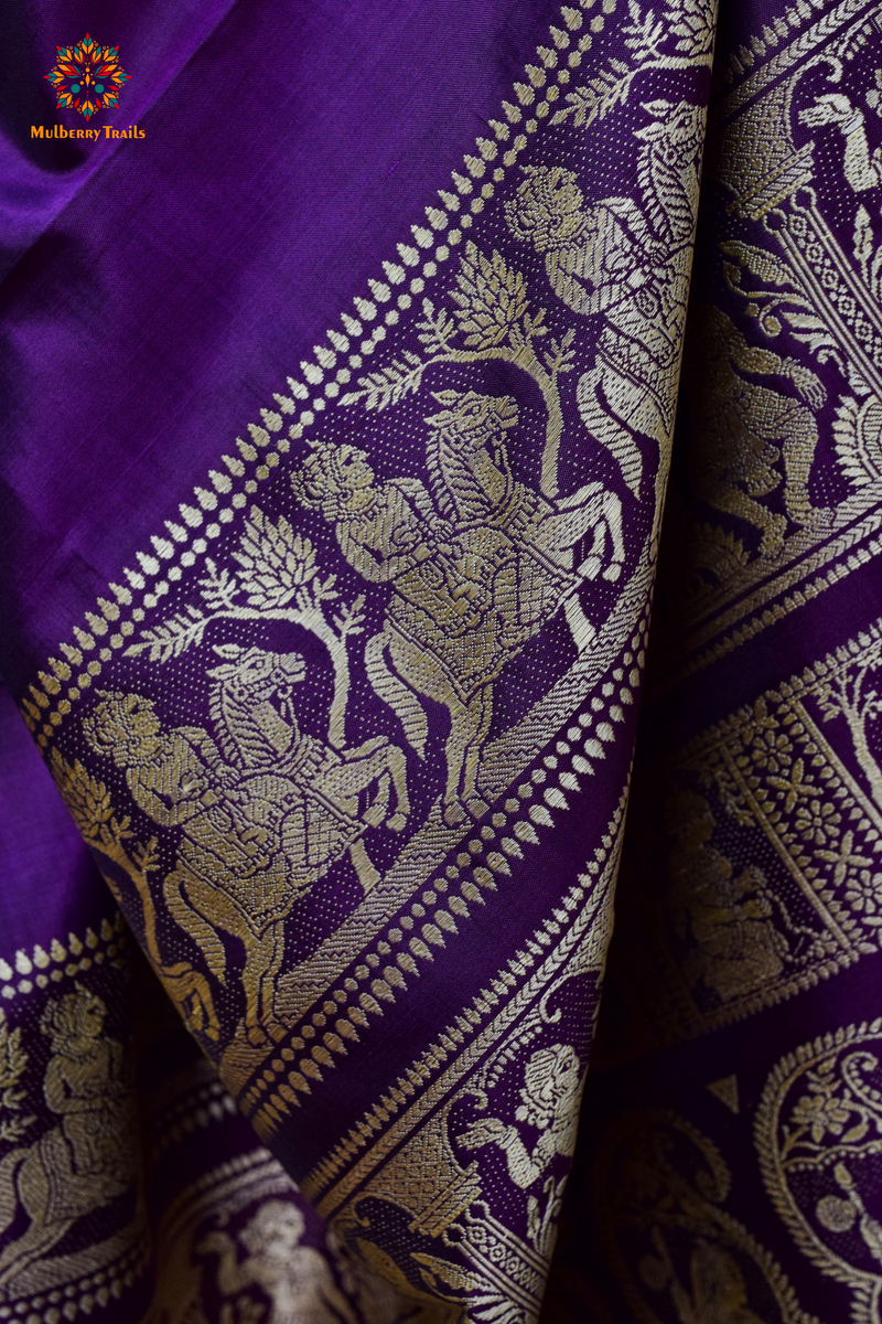 A woman wearing a Purple Baluchari Pure SIlk saree. purple baluchari silk , bengal silk saree with deer motif on pallu and ramayan, mahabharat motifs on pallu. This is a soft pure silk saree suitable for weddings, parties, festivities. suitable for Durga Puja shopping enthusiasts and diwali festival. 