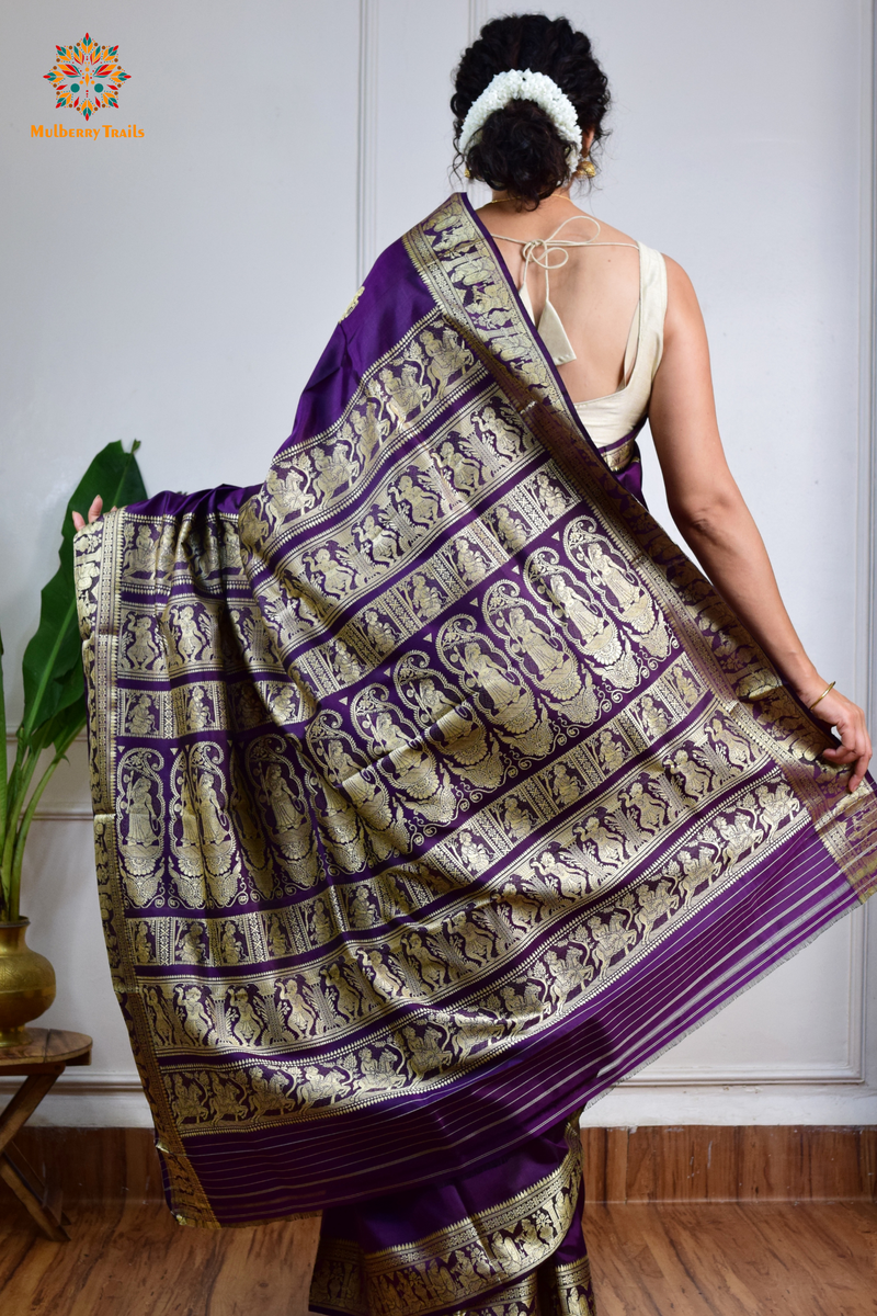 A woman wearing a Purple Baluchari Pure SIlk saree. purple baluchari silk , bengal silk saree with deer motif on pallu and ramayan, mahabharat motifs on pallu. This is a soft pure silk saree suitable for weddings, parties, festivities. suitable for Durga Puja shopping enthusiasts and diwali festival. 