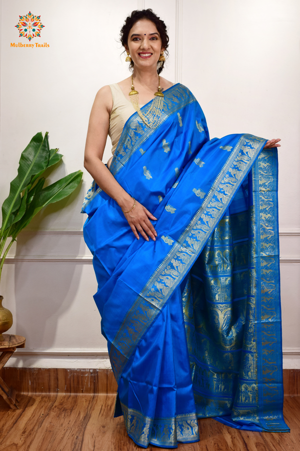 A woman wearing a Blue Baluchari Pure SIlk saree. Blue baluchari silk , bengal silk saree with deer motif on pallu and ramayan, mahabharat motifs on pallu. This is a soft pure silk saree suitable for weddings, parties, festivities. suitable for Durga Puja shopping enthusiasts and diwali festival. 