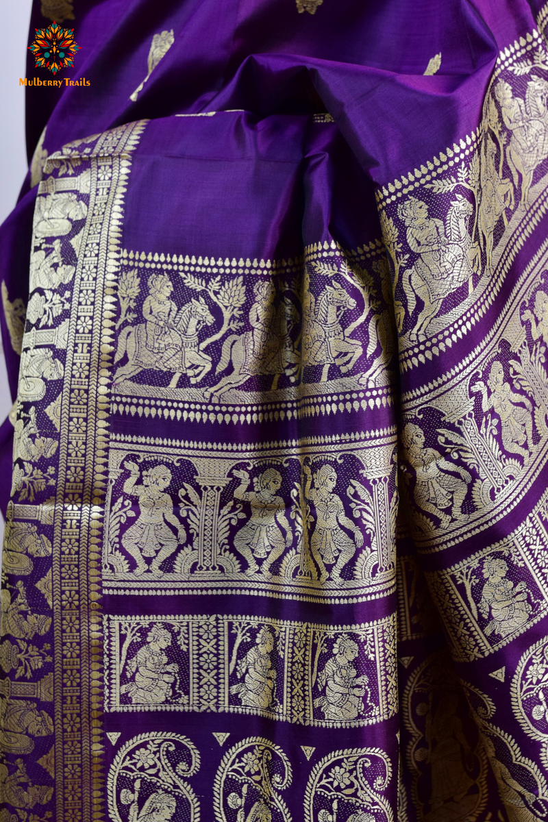 A woman wearing a Purple Baluchari Pure SIlk saree. purple baluchari silk , bengal silk saree with deer motif on pallu and ramayan, mahabharat motifs on pallu. This is a soft pure silk saree suitable for weddings, parties, festivities. suitable for Durga Puja shopping enthusiasts and diwali festival. 