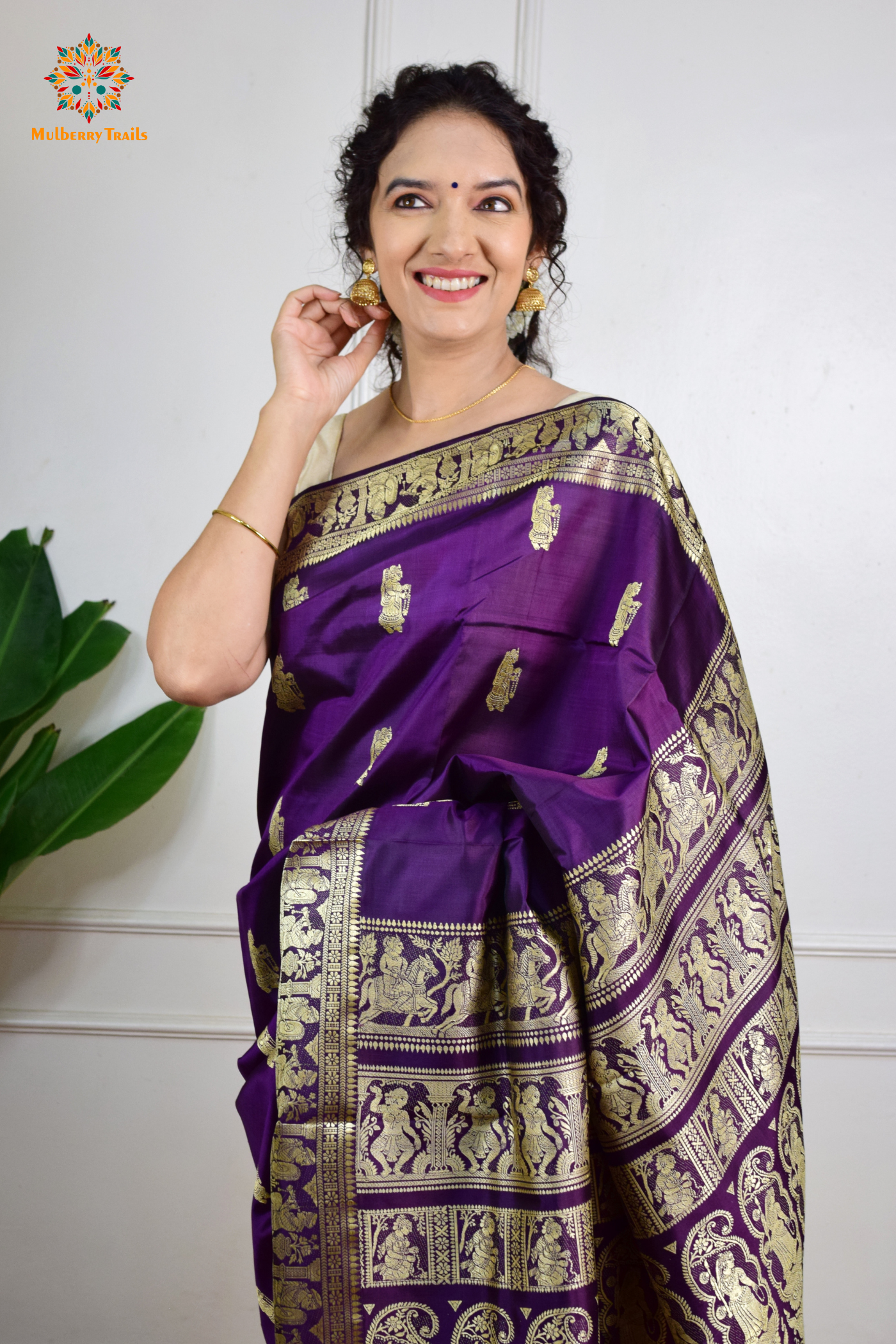 A woman wearing a Purple Baluchari Pure SIlk saree. purple baluchari silk , bengal silk saree with deer motif on pallu and ramayan, mahabharat motifs on pallu. This is a soft pure silk saree suitable for weddings, parties, festivities. suitable for Durga Puja shopping enthusiasts and diwali festival. 