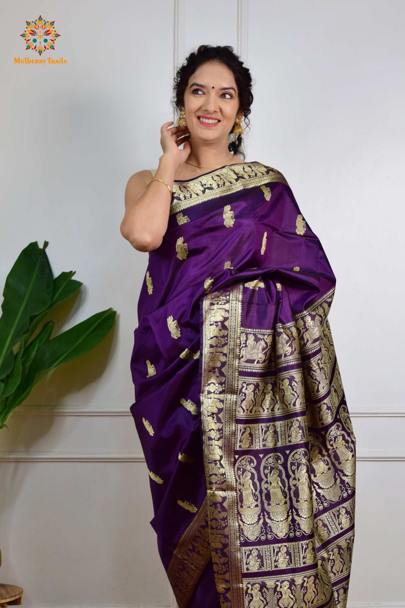 A woman wearing a Purple Baluchari Pure SIlk saree. purple baluchari silk , bengal silk saree with deer motif on pallu and ramayan, mahabharat motifs on pallu. This is a soft pure silk saree suitable for weddings, parties, festivities. suitable for Durga Puja shopping enthusiasts and diwali festival. 