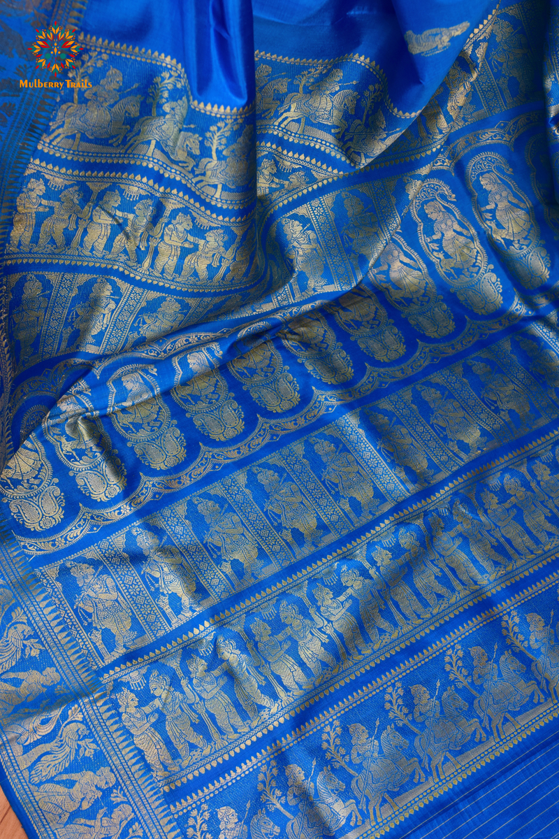 A woman wearing a Blue Baluchari Pure SIlk saree. Blue baluchari silk , bengal silk saree with deer motif on pallu and ramayan, mahabharat motifs on pallu. This is a soft pure silk saree suitable for weddings, parties, festivities. suitable for Durga Puja shopping enthusiasts and diwali festival. 