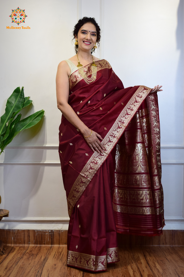 A woman wearing a Maroon Baluchari Pure SIlk saree. Maroon baluchari silk , bengal silk saree with deer motif on pallu and ramayan, mahabharat motifs on pallu. This is a soft pure silk saree suitable for weddings, parties, festivities. suitable for Durga Puja shopping enthusiasts and diwali festival. 