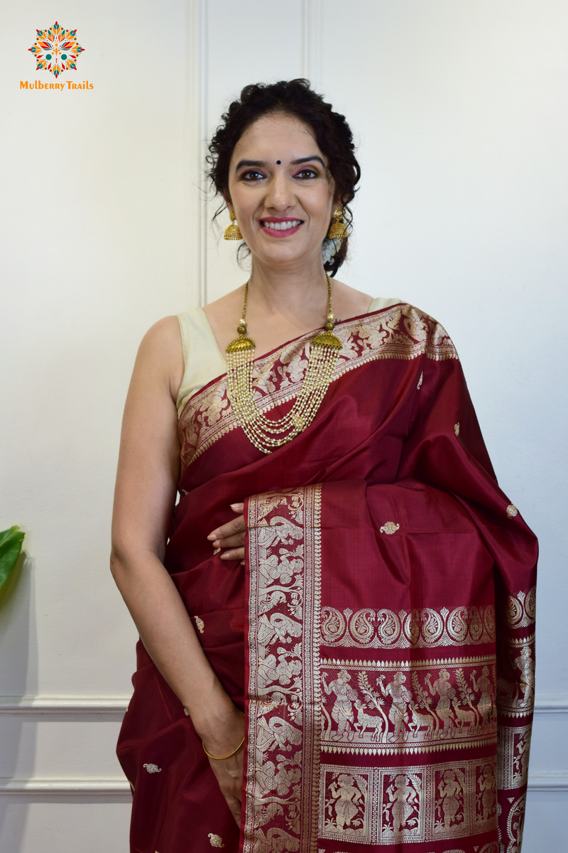 A woman wearing a Maroon Baluchari Pure SIlk saree. Maroon baluchari silk , bengal silk saree with deer motif on pallu and ramayan, mahabharat motifs on pallu. This is a soft pure silk saree suitable for weddings, parties, festivities. suitable for Durga Puja shopping enthusiasts and diwali festival. 