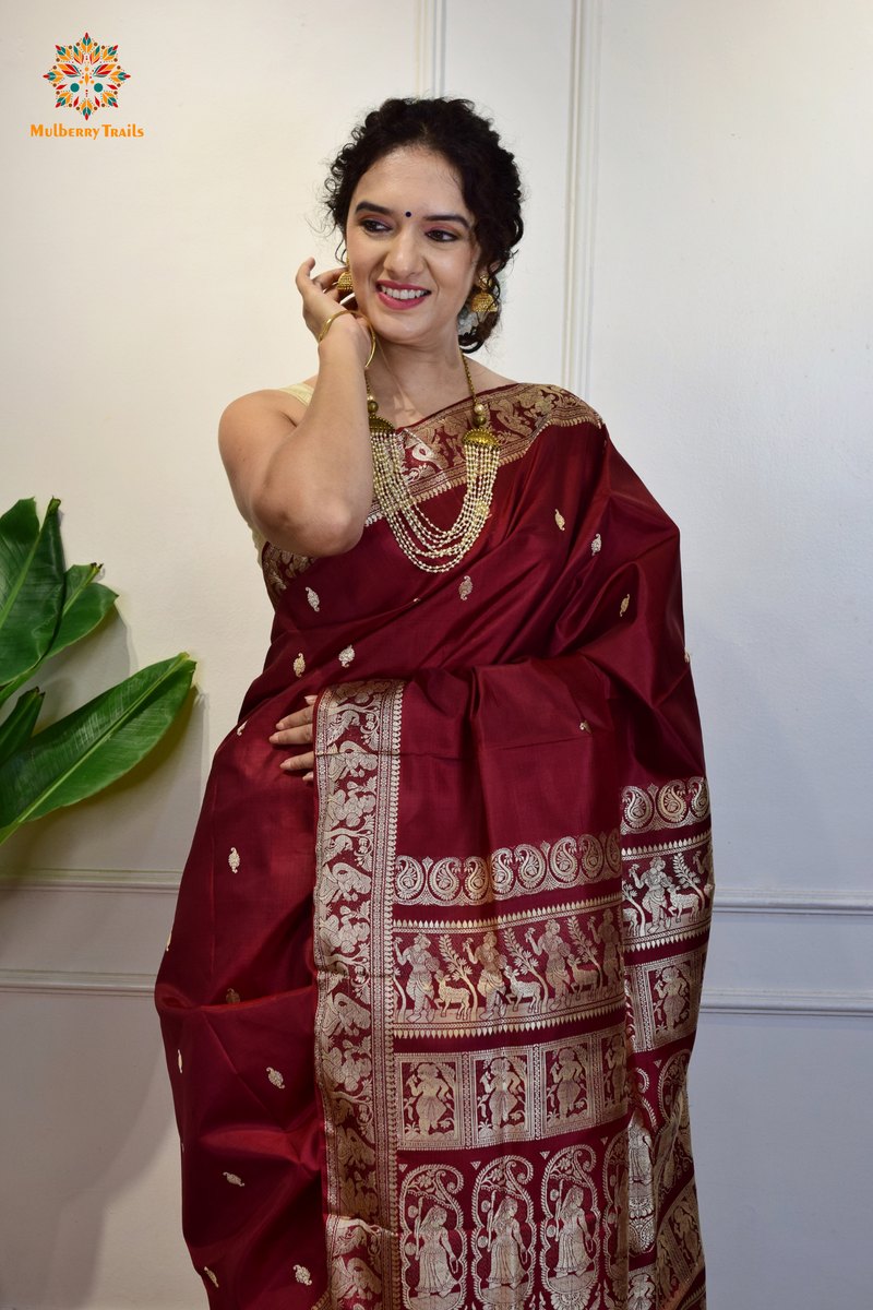 A woman wearing a Maroon Baluchari Pure SIlk saree. Maroon baluchari silk , bengal silk saree with deer motif on pallu and ramayan, mahabharat motifs on pallu. This is a soft pure silk saree suitable for weddings, parties, festivities. suitable for Durga Puja shopping enthusiasts and diwali festival. 