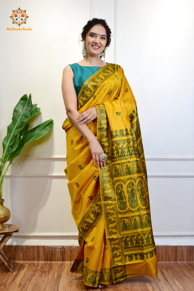 A woman wearing a Yellow Baluchari Pure SIlk saree. purple baluchari silk , bengal silk saree with deer motif on pallu and ramayan, mahabharat motifs on pallu. This is a soft pure silk saree suitable for weddings, parties, festivities. suitable for Durga Puja shopping enthusiasts and diwali festival. 