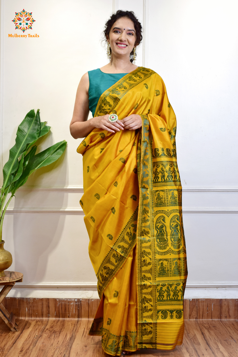 A woman wearing a Yellow Baluchari Pure SIlk saree. purple baluchari silk , bengal silk saree with deer motif on pallu and ramayan, mahabharat motifs on pallu. This is a soft pure silk saree suitable for weddings, parties, festivities. suitable for Durga Puja shopping enthusiasts and diwali festival. 