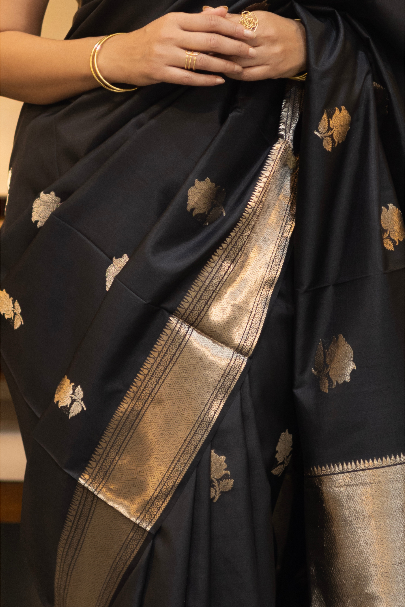 Woman in a black saree with gold patterns sitting indoor. Woman wearing a traditional baluchari saree in a room with a desk and lamp. Woman in a carrot red and silver resham work saree standing indoors with a desk and lamp in the background.

Baluchari – Pure Silk Baluchari Saree

1. “Pure silk Baluchari saree with temple motif weave and Silver resham detailing for a regal look.”

2. “Silk Mark pure silk saree featuring intricate gold resham work motifs and rich texture. 